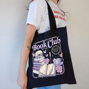 May include: Black tote bag with a graphic design featuring a skull, books, butterflies, and teacup. The text reads "Book Club" and "Making Friends With Characters, Not People."