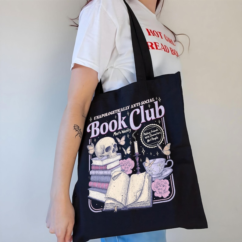 May include: Black tote bag with a graphic design featuring a skull, books, butterflies, and teacup. The text reads "Book Club" and "Making Friends With Characters, Not People."