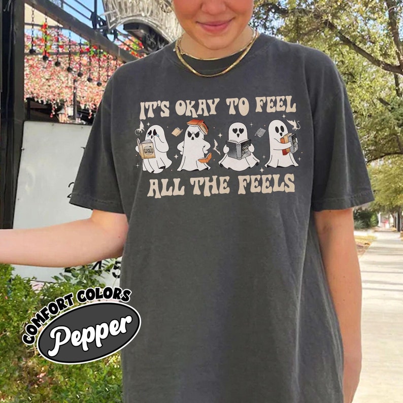 May include: A dark gray t-shirt with the text "It's okay to feel all the feels" and a line of four ghosts with different expressions. Each ghost is holding a book or a cup of coffee.