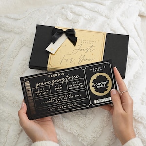 May include: A black gift box with a gold label reading Something Special Just For You and a black ribbon, paired with a black concert ticket card featuring gold text, a scratch-to-reveal circle, and details for Freddie at O2 Apollo Manchester.