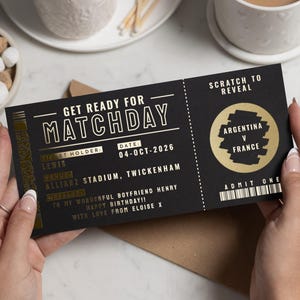 May include: A black ticket with gold lettering and accents, held by a person. The ticket reads "GET READY FOR MATCHDAY" and includes details for a match between Argentina and France. The date is October 4, 2026.