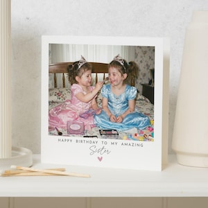 Könnte beinhalten: Eine quadratische Grußkarte mit einem Foto von zwei Kindern, die Diademe und Prinzessinnenkleider in Rosa und Blau tragen und mit Make-up spielen. Die Karte enthält den aufgedruckten Text: HAPPY BIRTHDAY TO MY AMAZING SISTER mit einem kleinen Herz.