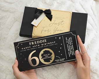 May include: A black gift box with a gold label reading "Something Special Just For You" and a black ribbon, paired with a black scratch-off ticket for a 60th birthday. The ticket features gold text "Freddie", "Happy 60th Birthday", and "Trip to the Highlands".