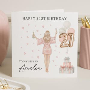 May include: A birthday card with the text "HAPPY 21ST BIRTHDAY" and "TO MY SISTER Amelia". The illustration shows a woman in a pink robe holding a bottle and a glass, with balloons and gifts. Pink hearts are scattered around the card.