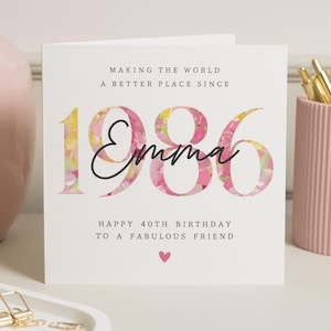 Op de afbeelding: Een witte verjaardagskaart met de tekst "MAKING THE WORLD A BETTER PLACE SINCE 1986 Emma HAPPY 40TH BIRTHDAY TO A FABULOUS FRIEND" in zwart en roze. De cijfers "1986" zijn gevuld met een bloemmotief. Onderaan staat een roze hart.