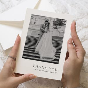 Peut inclure: Une carte de remerciement rectangulaire blanche avec une photographie en noir et blanc d'un couple debout sur des marches en pierre. Le texte THANK YOU est imprimé en noir, suivi des noms EMILY & ANTHONY et de la date 04.05.27 en police serif.