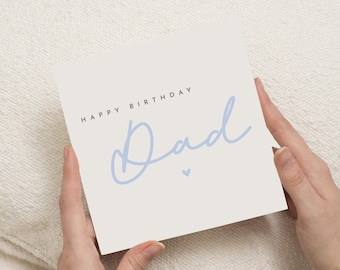 May include: A square greeting card with the words "HAPPY BIRTHDAY Dad" in black and light blue script. A small blue heart is below the word "Dad". The card is held by two hands.