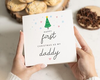 May include: A white card with a green Christmas tree and the text "Happy first Christmas as my daddy" in black and pink lettering.