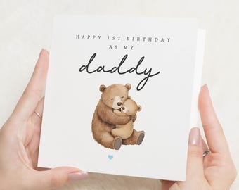 May include: A white birthday card with the words "HAPPY 1ST BIRTHDAY AS MY daddy" in black script. The card shows a watercolour illustration of two brown bears embracing. A small blue heart is at the bottom.