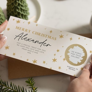 May include: A Christmas gift card with the name "Alexander" in elegant script. The card features gold star accents and the text "150 EUROS FOR YOUR HOLIDAY". The card is held by a person.