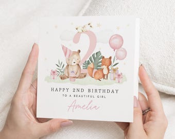 May include: A square birthday card with a watercolor illustration. The card features a bear with a party hat, a fox, and the number 2. The text reads "Happy 2nd Birthday to a Beautiful Girl" and the name "Amelia". Pink balloons and gifts are also shown.