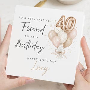 Op de afbeelding: Een vierkante witte verjaardagskaart met de tekst TO A VERY SPECIAL Friend ON YOUR Birthday, HAPPY BIRTHDAY en de naam Lucy. Het ontwerp bevat een tros roségouden en witte ballonnen met het getal 40 in roségoudfolie.
