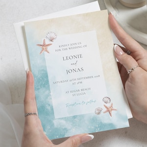 Puede incluir: Una invitación de boda con temática de playa. La invitación presenta un diseño de acuarela con tonos azules y beige, conchas marinas y estrellas de mar. El texto dice "Kindly join us for the wedding of Leonie and Jonas", incluyendo fecha, hora y lugar.