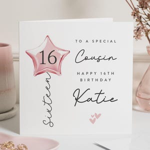 Op de afbeelding: Een witte wenskaart met een roze stervormige ballon met het nummer 16. De kaart leest "To a special Cousin, Happy 16th Birthday Katie" en heeft twee kleine roze hartjes. Het woord "Sixteen" is verticaal geschreven.