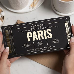 May include: A black boarding pass with gold detailing, announcing a trip to "PARIS". The pass includes the date, time, and departure airport, with the message "Happy Birthday! Have the best time" at the bottom.