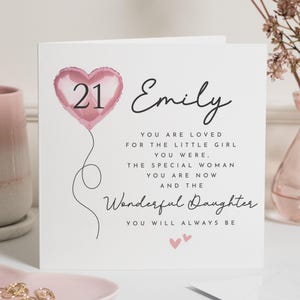 May include: A white birthday card featuring a pink heart-shaped balloon with the number 21. The card is personalized with the name "Emily" and a loving message. A perfect card for a 21st birthday.