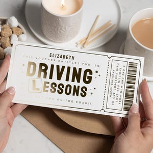 May include: A driving lessons gift voucher in white and gold. The voucher says "DRIVING LESSONS" in gold lettering, with the recipient's name, "ELIZABETH", at the top. It includes a barcode and a birthday message.