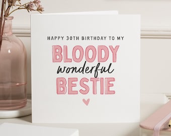 May include: A white square greeting card with the text "HAPPY 30TH BIRTHDAY TO MY BLOODY wonderful BESTIE" in pink and black lettering. A small pink heart is at the bottom. A pink vase with flowers is in the background.