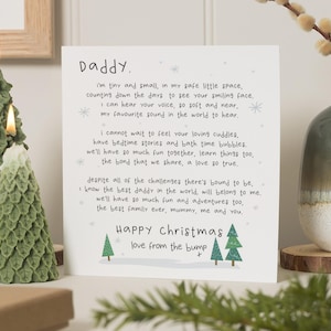 May include: A white greeting card featuring black printed text addressed to Daddy, including a poem about a baby in the womb, with small green Christmas tree illustrations at the bottom and the text Happy Christmas love from the bump.
