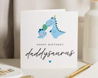 May include: A white card with a blue dinosaur and a smaller blue dinosaur holding a green balloon. The text on the card reads "Happy Birthday Daddysaurus".