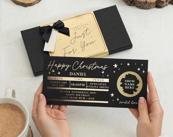 May include: A black rectangular gift box with a gold label reading "Something Special Just For You" and a black ribbon, paired with a black ticket-style card featuring gold text "Happy Christmas," "Daniel," event details, and a scratch-off circle.