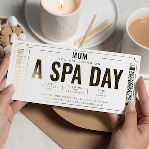 May include: A spa day ticket with the text "MUM YOU ARE GOING ON A SPA DAY". The ticket is white with gold accents and includes the date, location, and time. The ticket is held by a person.
