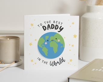 May include: A white greeting card with the text "TO THE BEST DADDY IN THE World". The card features a blue and green illustrated globe with a smiling face. Yellow stars are scattered around the text and globe.
