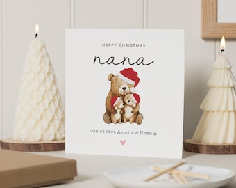 May include: A Christmas card with a watercolor illustration of a bear family wearing Santa hats. The card reads "Happy Christmas Nana" with "lots of love Amelia & Noah x" below. Two tree-shaped candles flank the card.