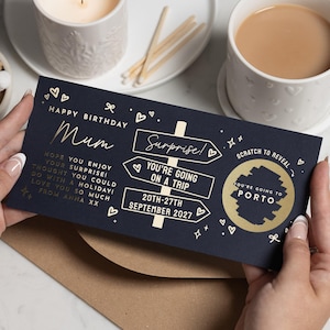 May include: A dark blue rectangular scratch-off card featuring gold foil text and graphics. The card reads Happy Birthday Mum, Surprise! You're going on a trip, 20th-27th September 2027, and includes a gold scratch-off circle revealing Porto.