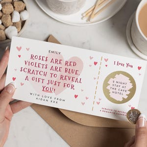 May include: A white gift card with pink hearts and text that reads "Roses are red, violets are blue, scratch to reveal a gift just for you!" A gold scratch-off area reveals a 2-night stay at a hotel. A coin is held near the scratch-off area.