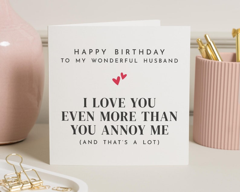 May include: A white card with black text that reads "Happy Birthday to my wonderful husband. I love you even more than you annoy me (and that's a lot)". There are two small red hearts above the text.