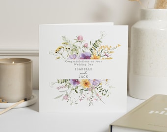Op de afbeelding: Een witte kaart met een aquarel bloemenontwerp in tinten paars, geel en groen. De tekst luidt "Gefeliciteerd met jullie huwelijksdag Isabelle en Jack".