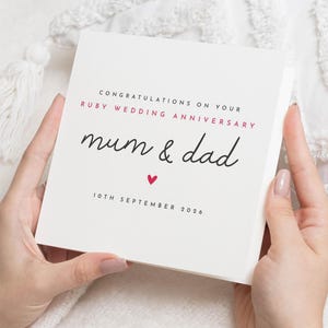 May include: A white square card with the text "Congratulations on your Ruby Wedding Anniversary mum & dad" in black script and red text. A small red heart is below the text. The date "10th September 2026" is printed at the bottom.