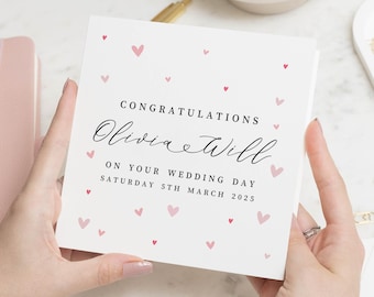 Op de afbeelding: Een vierkante witte trouwkaart met de tekst "Congratulations Olivia & Will" in sierlijke letters, versierd met roze hartjes. De datum "Zaterdag 5 maart 2025" staat er ook op.