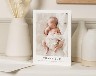 May include: A white thank you card with a photo of a baby sleeping on a white blanket with pink flowers. The text on the card reads "Thank You" with the baby's name, birthdate, and weight.