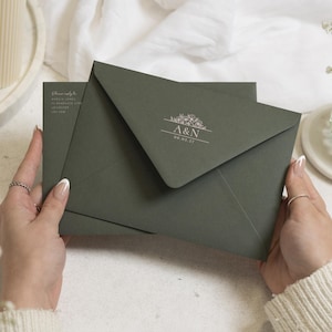 Op de afbeelding: Een donker olijfgroene envelop met een witte bloemafbeelding en de tekst A&N 08.05.27 op de klep. De envelop is gemaakt van mat papier en bevat een in het wit gedrukt retouradres in de linkerbovenhoek van het achterpaneel.