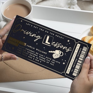 May include: A navy blue gift voucher for driving lessons. The voucher features gold lettering that reads "Driving Lessons" and includes the text "Happy Birthday!" and "Amelia Williams." The voucher also has a key and car graphic.