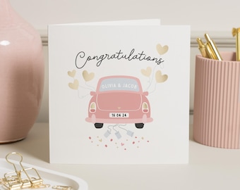 May include: A white card with the text "Congratulations" in black script. A pink car with gold hearts attached to the back is driving away. The car has a license plate that reads "16 04 24" and the text "Olivia & Jacob" on the back window.