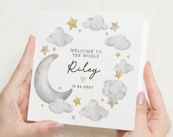 May include: A square greeting card with a watercolor design featuring a crescent moon, clouds, and stars. The text reads "WELCOME TO THE WORLD" above the name "Riley" and the date "12.06.2025". The card is held by a person.