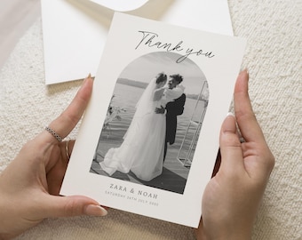 May include: A thank you card held by hands, featuring a black and white photo of a couple embracing. The card reads "Thank you" in script above the photo, with the names "ZARA & NOAH" and the date "SATURDAY 26TH JULY 2025" below.