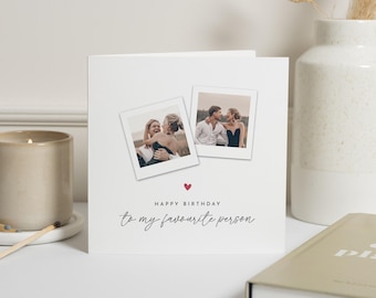 May include: A square white greeting card featuring two tilted square photo prints of a couple. Below the photos is a small red heart icon and the black printed text: HAPPY BIRTHDAY to my favourite person. The card has a clean, minimalist design.