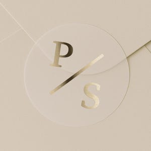 May include: A transparent, circular sticker with gold foil lettering. The sticker displays the letters "P" and "S" with a diagonal line. It's placed on a light beige envelope, creating a minimalist design.