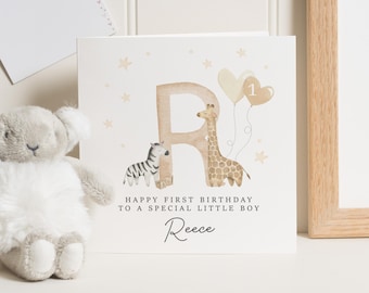 Puede incluir: Una tarjeta blanca con una ilustración de jirafa y cebra marrones. La tarjeta dice "Happy First Birthday to a Special Little Boy Reece".