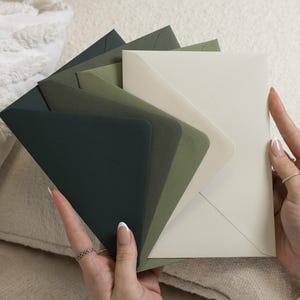 Op de afbeelding: Een set van vijf rechthoekige papieren enveloppen in een waaieropstelling, met een kleurverloop van donker bosgroen naar olijfgroen, saliegroen en een lichte crème-witte tint, elk voorzien van een puntige driehoekige sluiting.