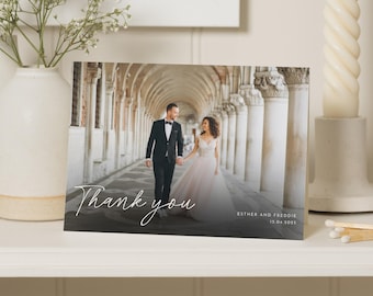 May include: A wedding thank you card with a photo of a bride and groom in a white archway. The text "Thank you" is written in white script on a black background. The card also includes the names "Esther and Freddie" and the date "15.04.2023".