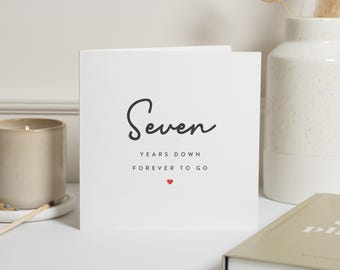 Peut inclure: Carte blanche avec du texte noir qui dit "Seven Years Down Forever To Go" avec un petit symbole de cœur rouge.