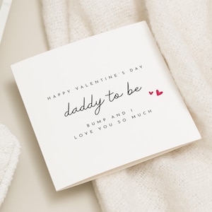 May include: A white Valentine's Day card with the text "Happy Valentine's Day daddy to be" in black script. The card also includes the phrases "Bump and I love you so much" and two small red hearts.