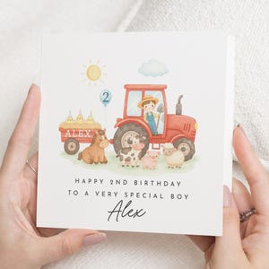 Op de afbeelding: Verjaardagskaart met een rode tractor, een boer en boerderijdieren. De kaart zegt "Gelukkige 2e verjaardag voor een heel bijzondere jongen" en bevat de naam "Alex". Een zon en een ballon met het nummer 2 zijn ook afgebeeld.