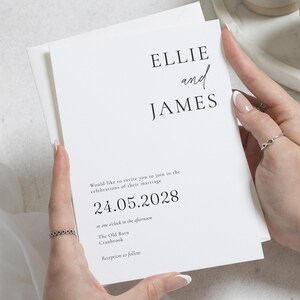 Puede incluir: Una invitación de boda blanca con los nombres "ELLIE and JAMES" en negro. La invitación incluye la fecha "24.05.2028" y detalles del evento. La invitación está sostenida en las manos de una persona.