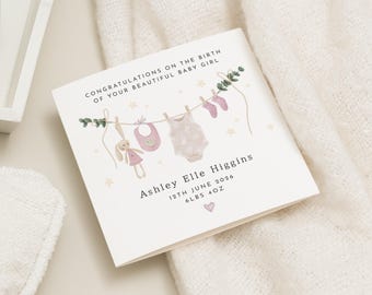 May include: A white card with the text "CONGRATULATIONS ON THE BIRTH OF YOUR BEAUTIFUL BABY GIRL". The card features illustrations of baby clothes, a bunny, and the name "Ashley Elle Higgins". The card also includes the date "12TH JUNE 2026" and the weight "6LBS 4OZ".